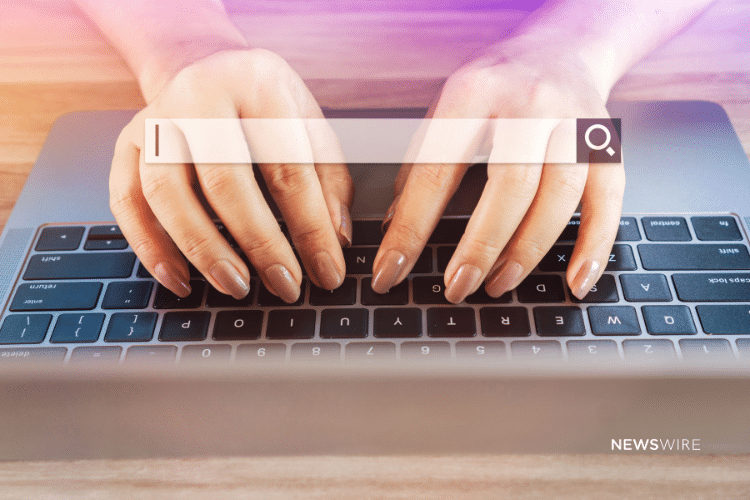 Picture of a woman's hands with light brown painted fingernails on a MacBook keyboard with a search engine search bar overlayed. Image is being used for a Newswire blog about SEO and press release distribution.