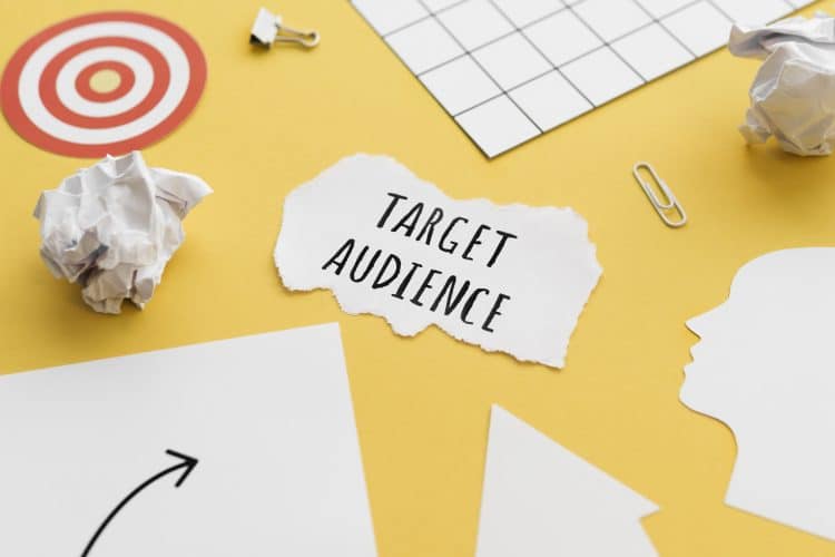 "Target Audience" is written on a scrap of paper on a yellow table top with other pieces of paper