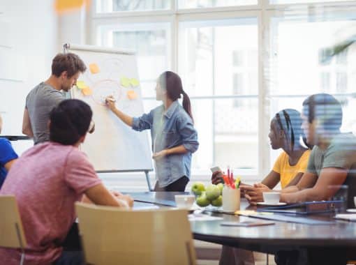 Business executives discussing with their colleagues on whiteboard during meeting at office - Picture being used for a blog about Newswire helping tech CEOs earn media mentions.