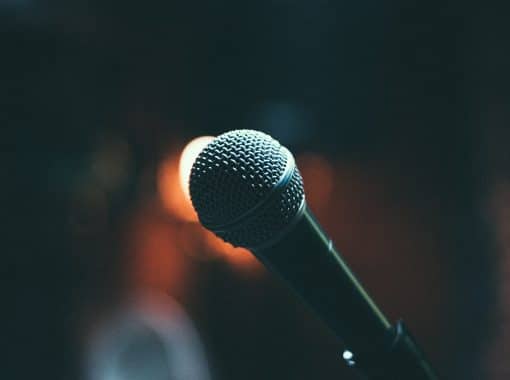Close-up picture of a microphone on stage. Image is being used for a blog post titled, "How Are Small and Midsize Companies Using this Marketing Strategy to Amplify Messaging?"