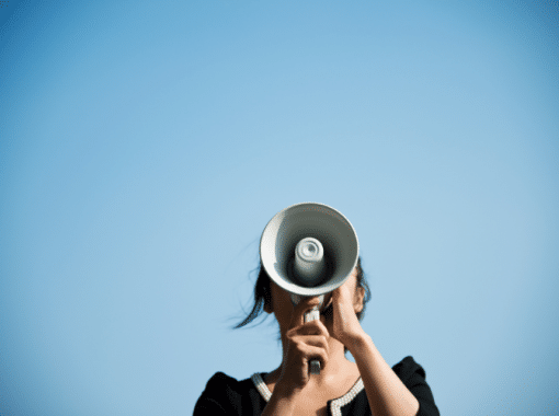 Image of a lady speaking into a megaphone with a blue sky background. Picture is being used for a blog post about press release campaigns.