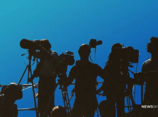 Shadows of media personnel with cameras on a blue backdrop. Image is being used for a Newswire blog about handling negative publicity.