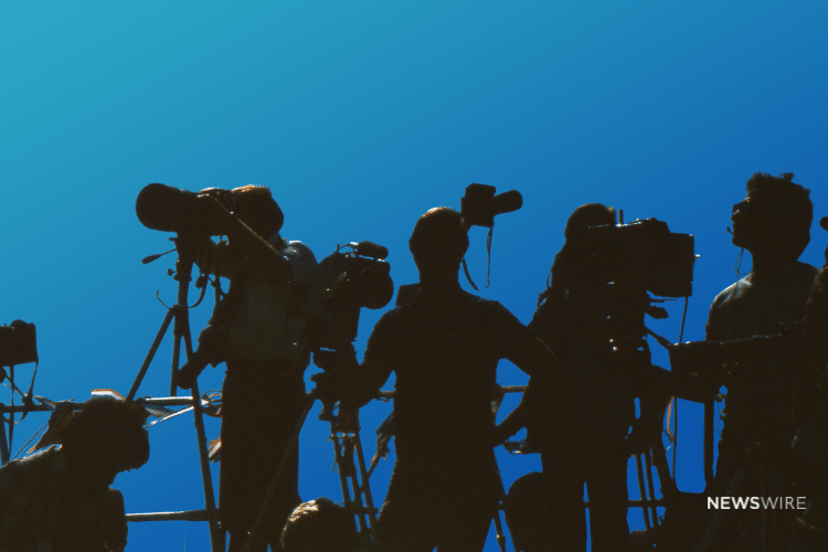 Shadows of media personnel with cameras on a blue backdrop. Image is being used for a Newswire blog about handling negative publicity.