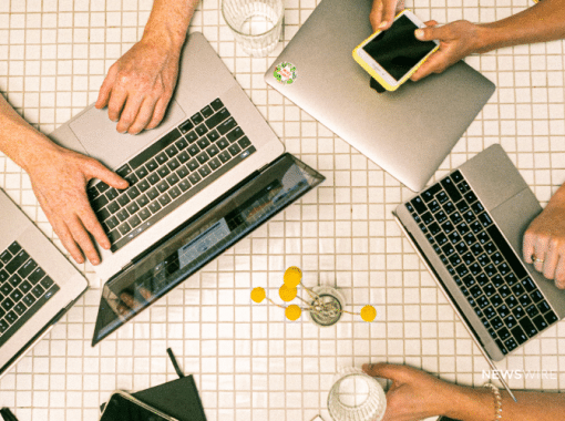 Overhead picture of people working on Macbook computers and an iPhone. Image is being used for a Newswire blog post about press release distribution best practices.