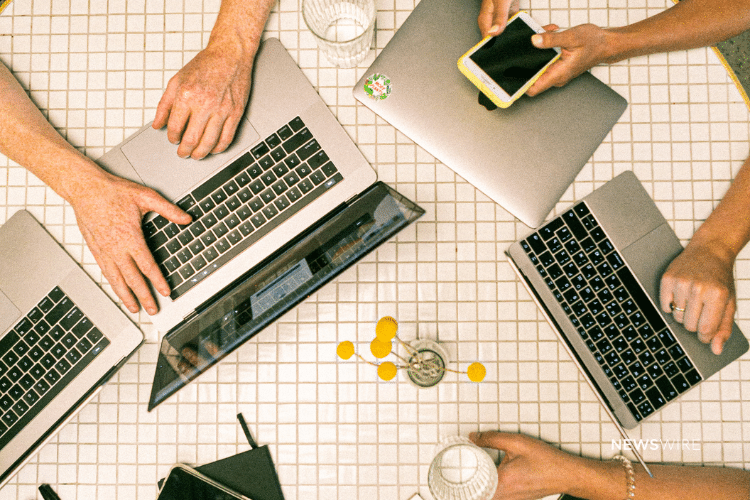 Overhead picture of people working on Macbook computers and an iPhone. Image is being used for a Newswire blog post about press release distribution best practices.