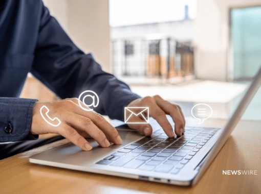 Picture of a man in a blue button down typing on a computer. There are four symbols near his hands, telephone symbol, ampersand, an envelope, and a speech bubble. Image is being used for a Newswire blog about a Media Database.