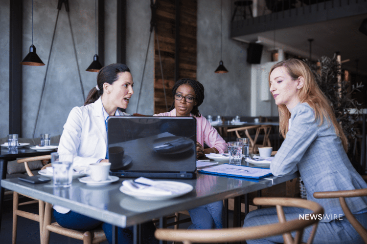 Picture of three business women in a coffee shop sitting in front of a computer and talking. Image is being use for a Newswire blog about Media Pitching improving the effectiveness of press release distribution.