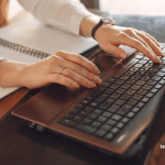 Picture of a woman wearing a white blouse typing on a computer. Image is being used for a Newswire blog about How to Get Journalist Attention.
