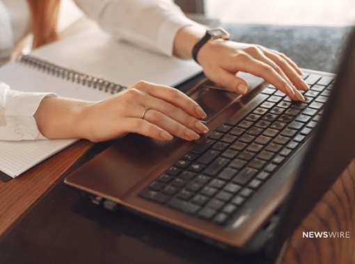 Picture of a woman wearing a white blouse typing on a computer. Image is being used for a Newswire blog about How to Get Journalist Attention.