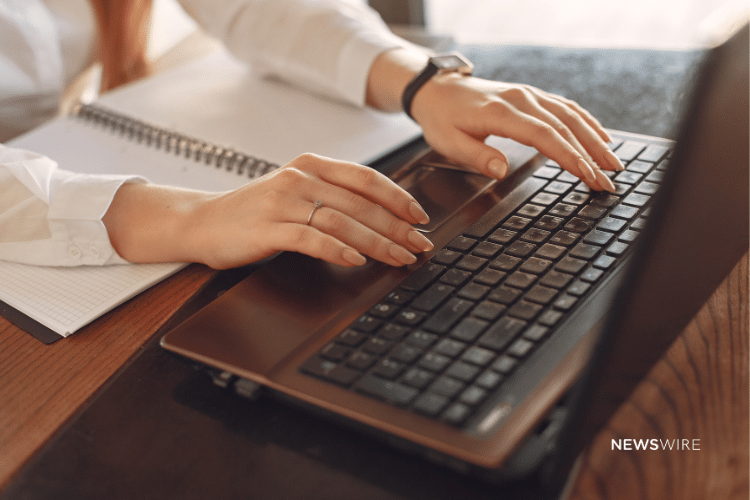 Picture of a woman wearing a white blouse typing on a computer. Image is being used for a Newswire blog about How to Get Journalist Attention.