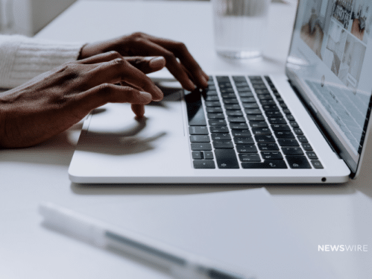 Newswire-branded image of an African American woman typing on a Macbook.