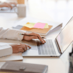 Picture of a lady's hands on a MacBook in a business setting.